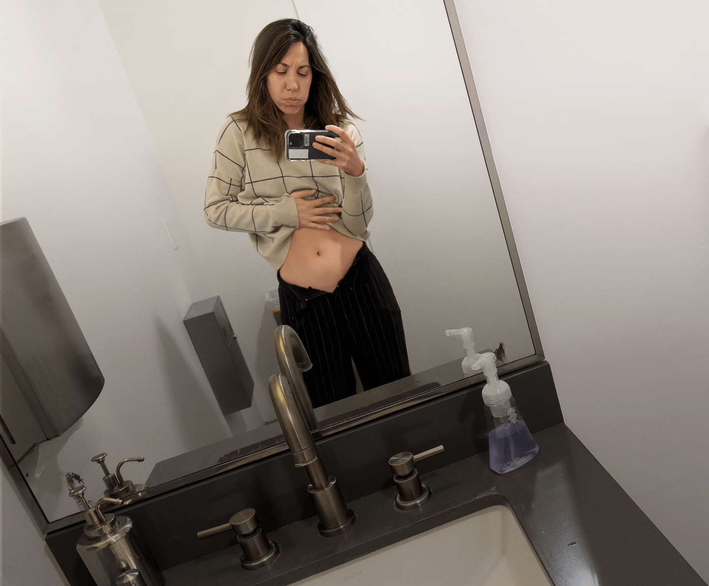 Actor portrayal of a woman living with endometriosis pain who is looking at her stomach in a bathroom mirror